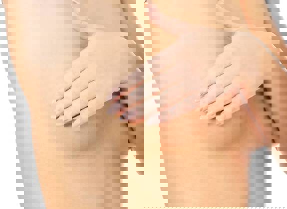 Close up of a woman performing a breast self-exam with one hand raised and the other gently checking the breast area