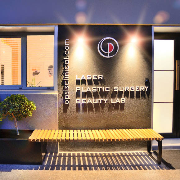 Evening exterior view of Opsis Clinical entrance, featuring laser and plastic surgery beauty lab signage